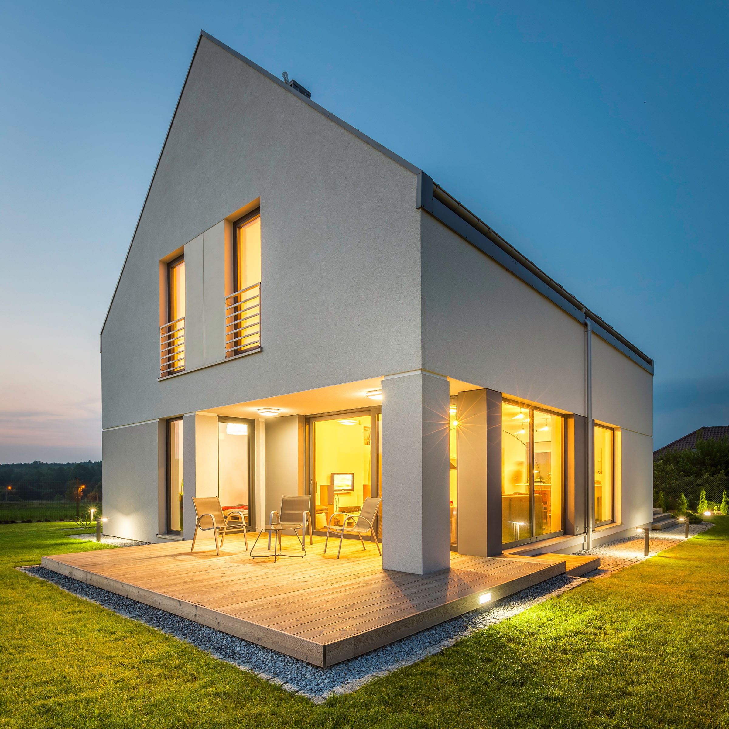 Modern house with illuminated decking and garden at dusk